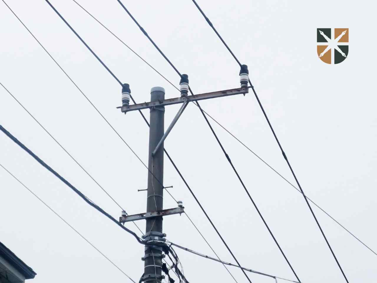 Słup energetyczny z liniami przesyłowymi i izolatorami na tle zachmurzonego nieba.