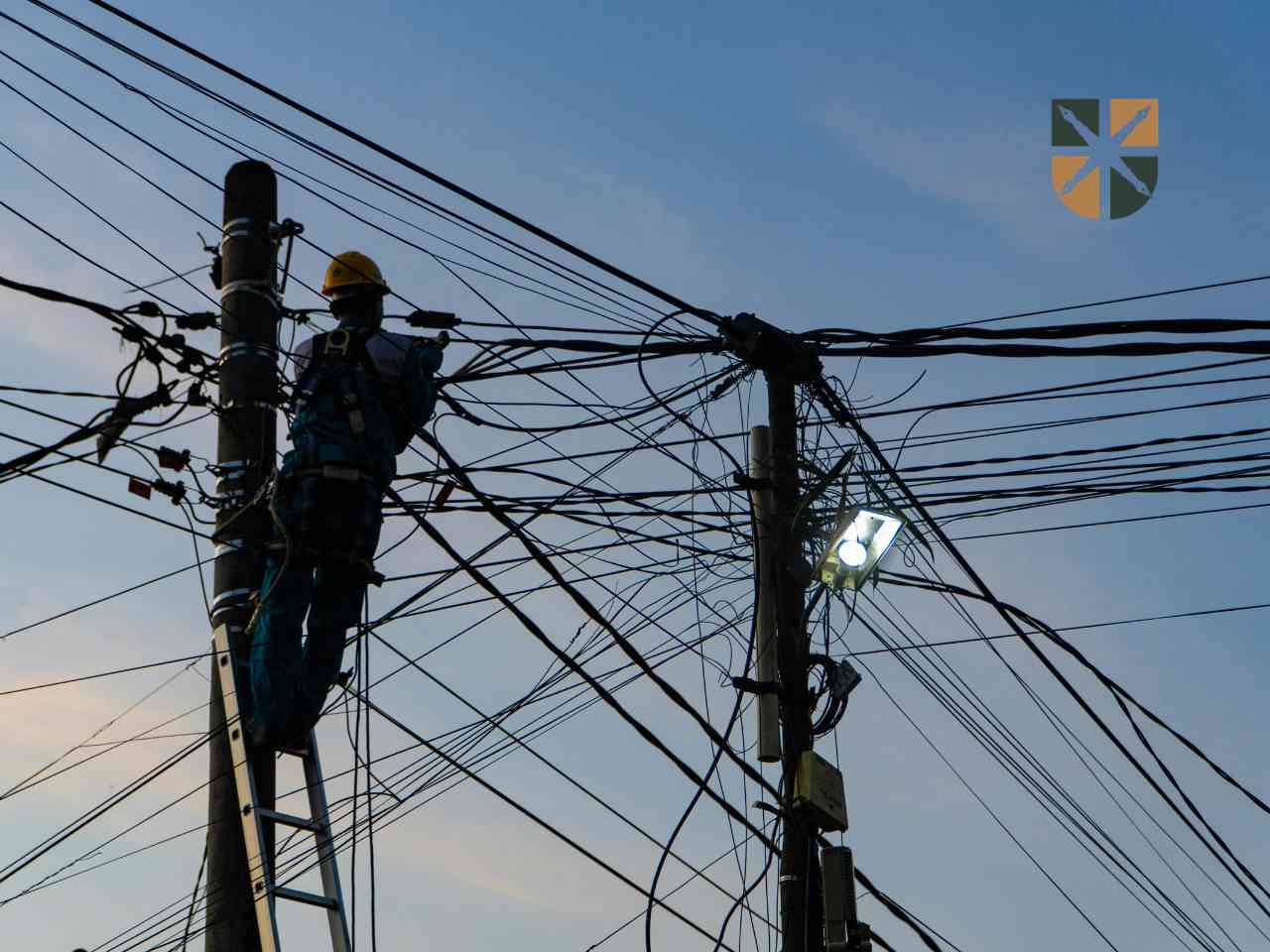 inżynier-linia-energetyczna Elektryk na drabinie naprawia gąszcz przewodów na słupie energetycznym, ilustrując modernizację sieci.