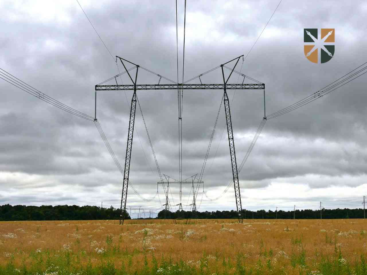 Metalowy słup wysokiego napięcia stoi na zaoranym polu, oznaczając pas służebności przesyłu na działce rolnika.