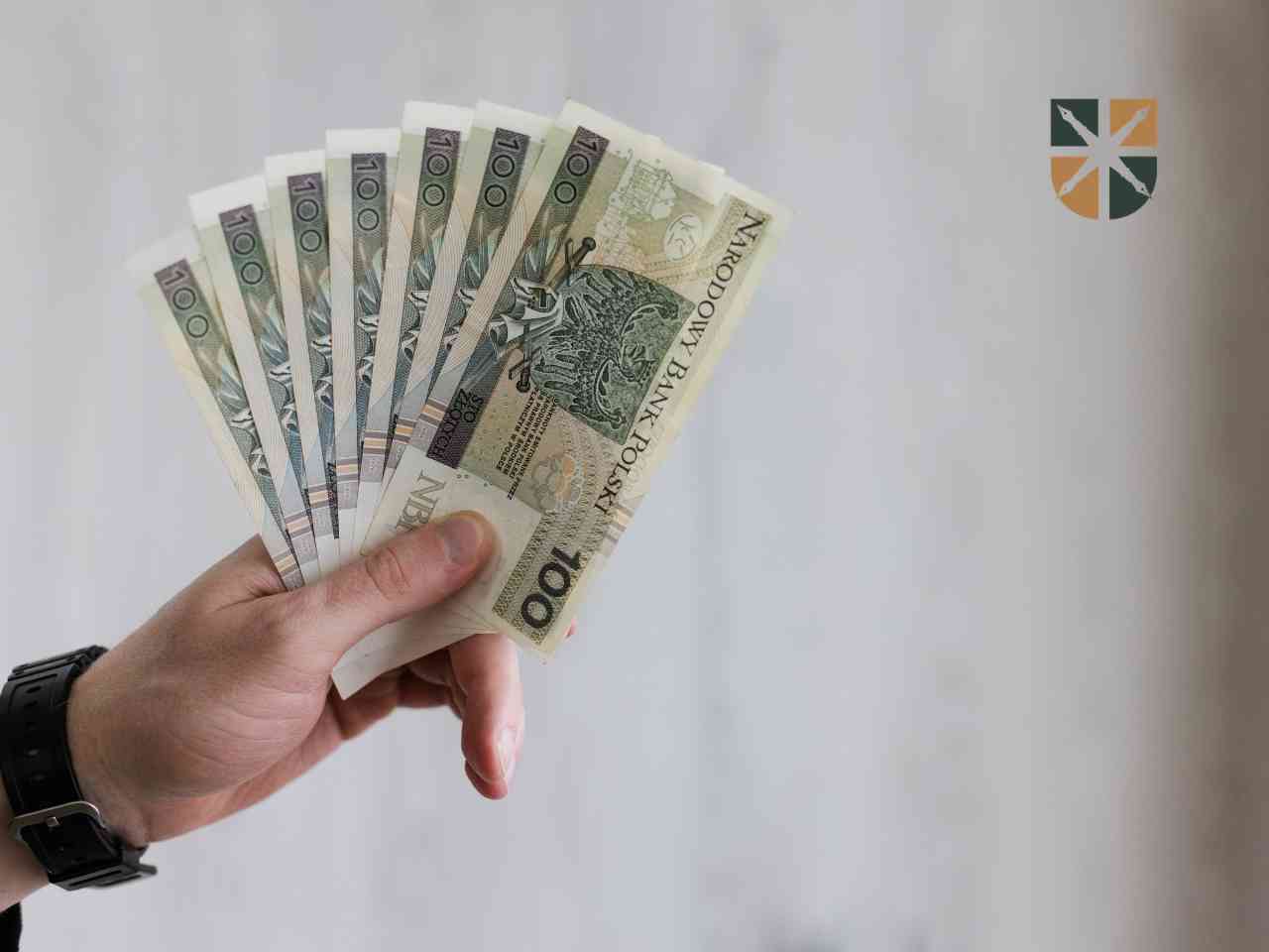 Dłoń trzymająca plik banknotów 100 zł – symbolizuje wypłatę odszkodowania z OC sprawcy.