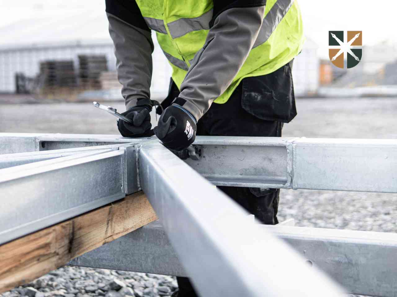 Pracownik w kamizelce odblaskowej skręca kluczem stalową konstrukcję nowego słupa elektroenergetycznego.