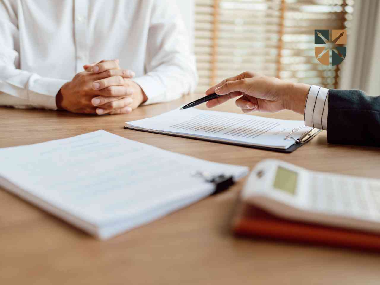 Two people sit at a wooden table reviewing a contract; one person points with a pen as the other watches.