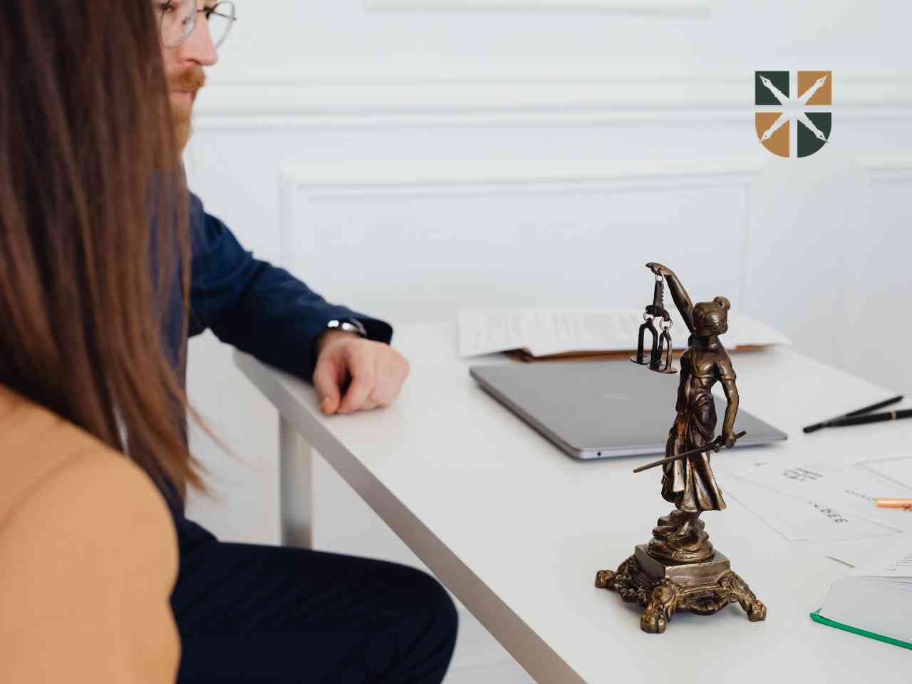 Adwokat rozmawia z klientką przy biurku obok figurki Temidy – profesjonalna pomoc prawna po wypadku.