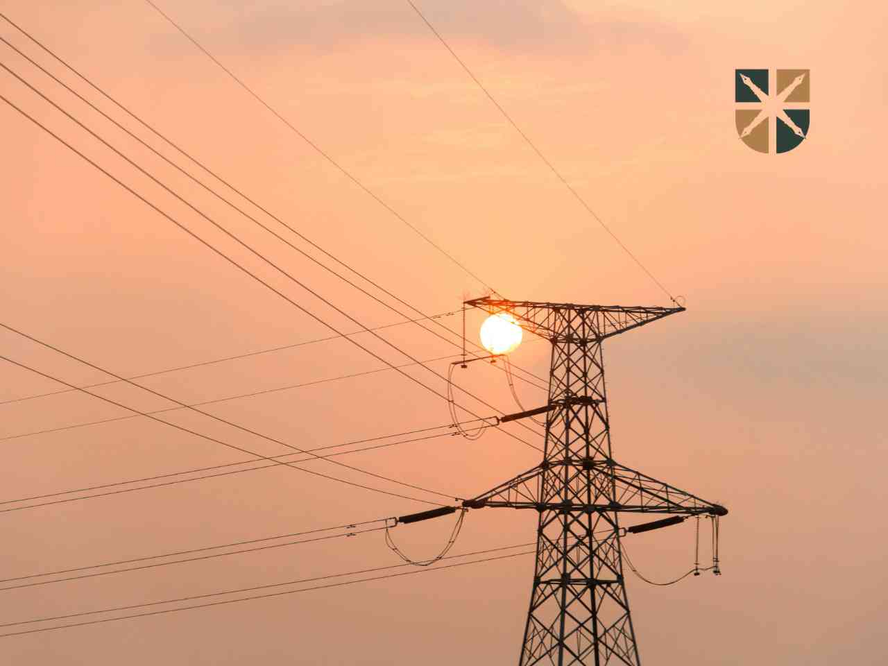 Stalowy słup linii elektroenergetycznej na tle pomarańczowego nieba o zachodzie słońca.