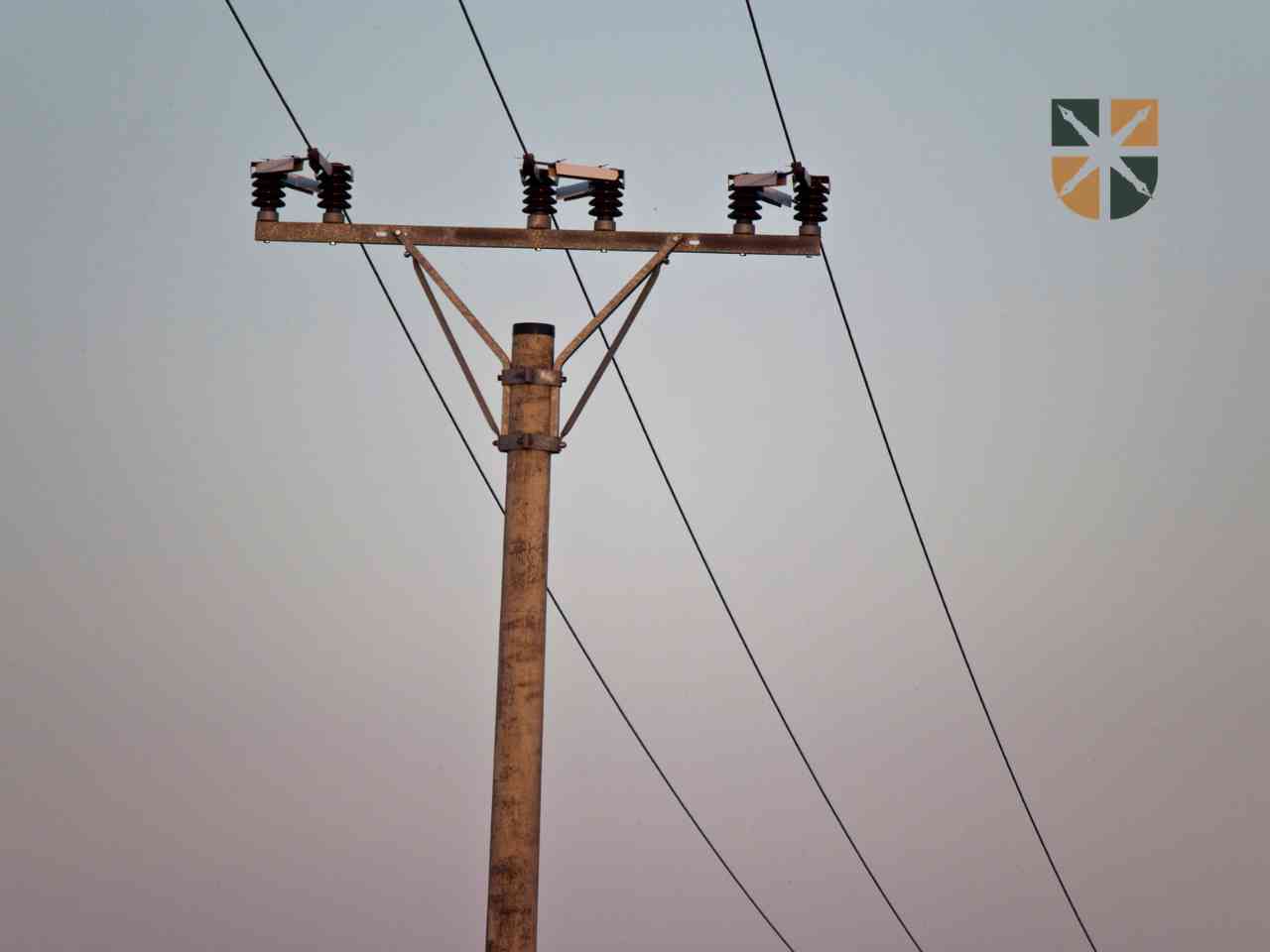 Betonowy słup energetyczny starego typu z izolatorami na tle nieba.