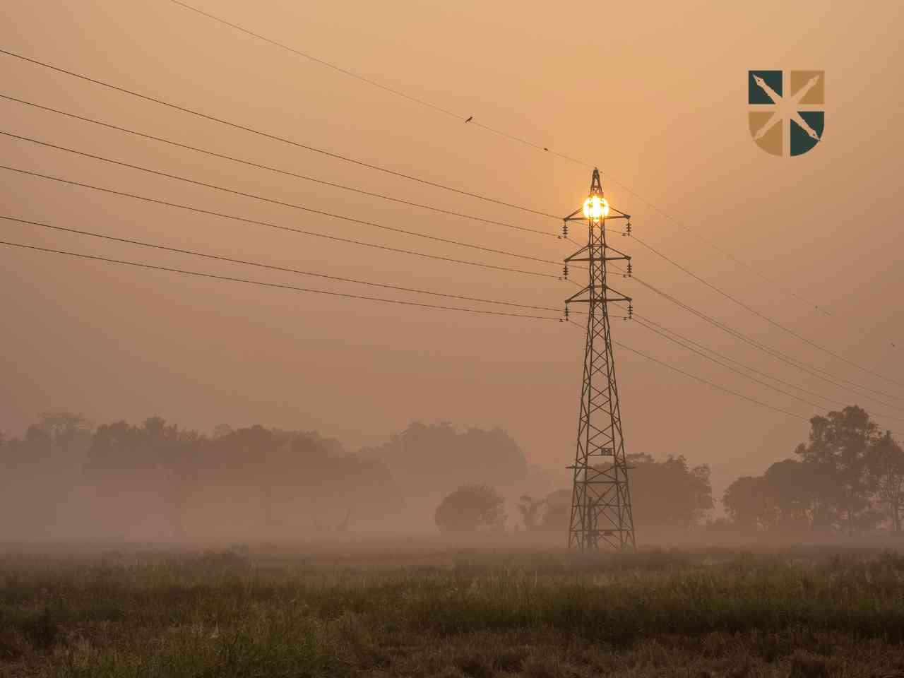 Metalowa wieża kratowa linii wysokiego napięcia w porannej mgle podczas wschodu słońca.