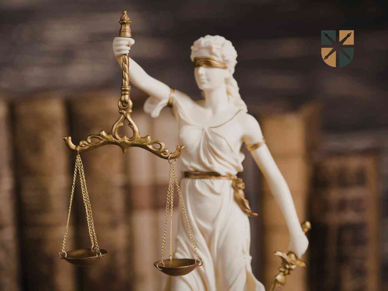 Statuetka Temidy z wagą na tle starych ksiąg prawniczych symbolizuje walkę o sprawiedliwość.