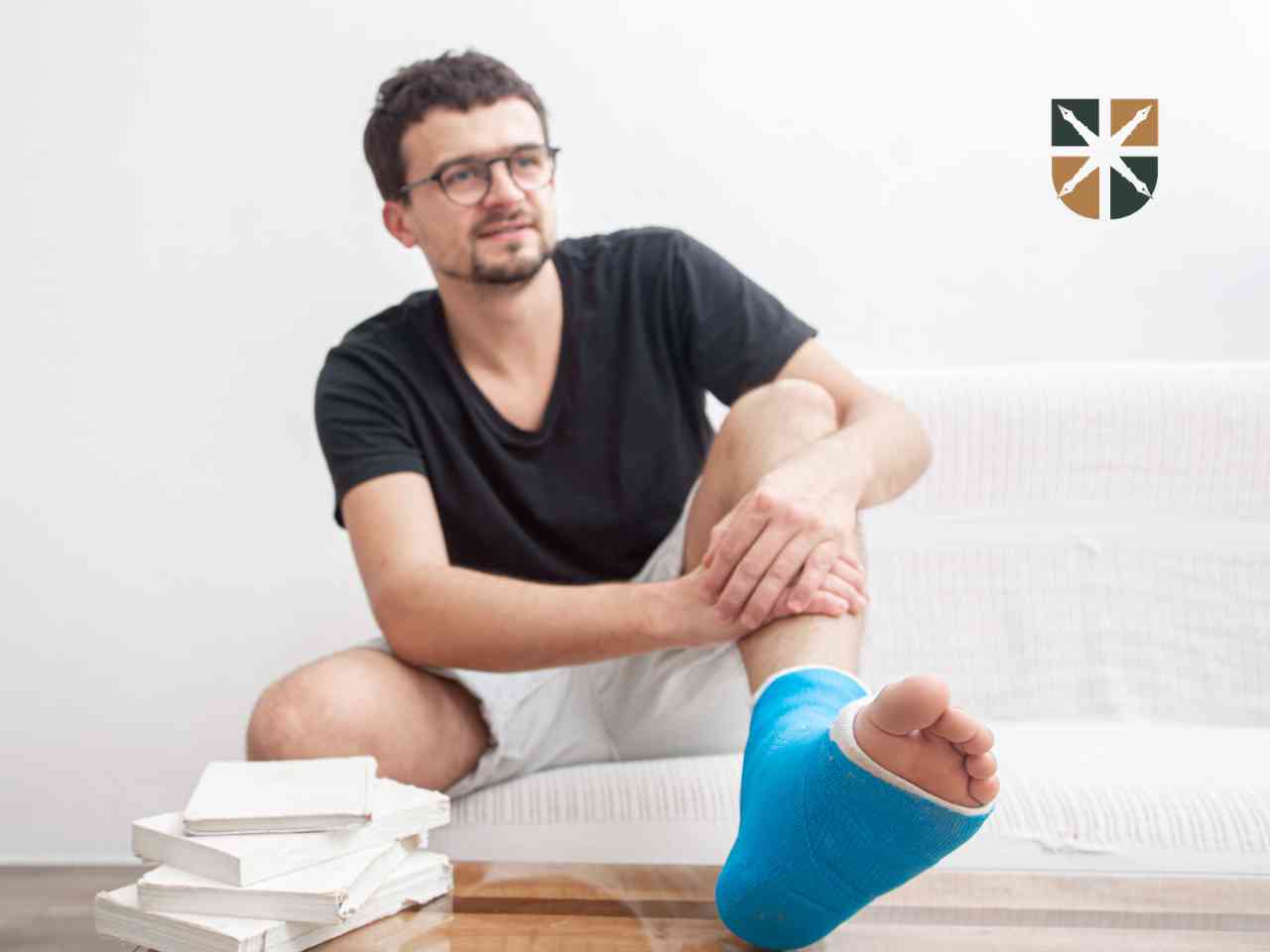Mężczyzna siedzący na kanapie z nogą w niebieskim gipsie – ilustracja uszczerbku na zdrowiu.