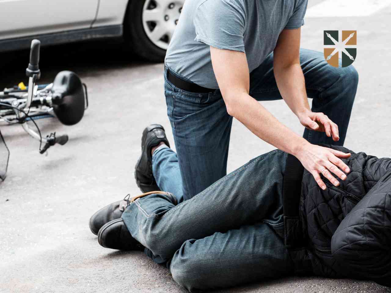 Świadek udzielający pomocy rowerzyście leżącemu na jezdni obok samochodu – przykład wypadku komunikacyjnego.
