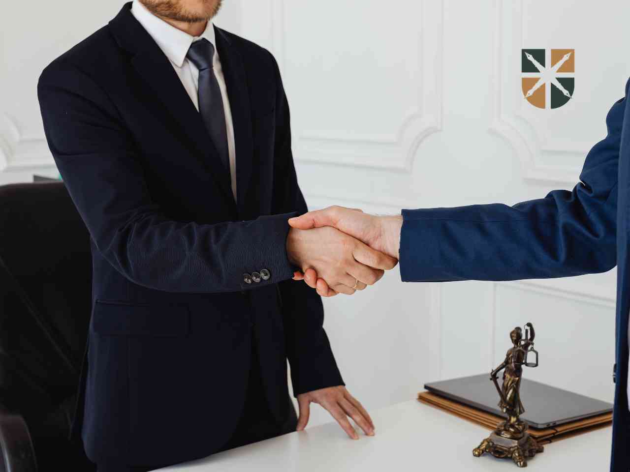 pomoc-prawnika-w-odwolaniu Two professionals shake hands across a white desk in a formal office, symbolizing an agreement or partnership.