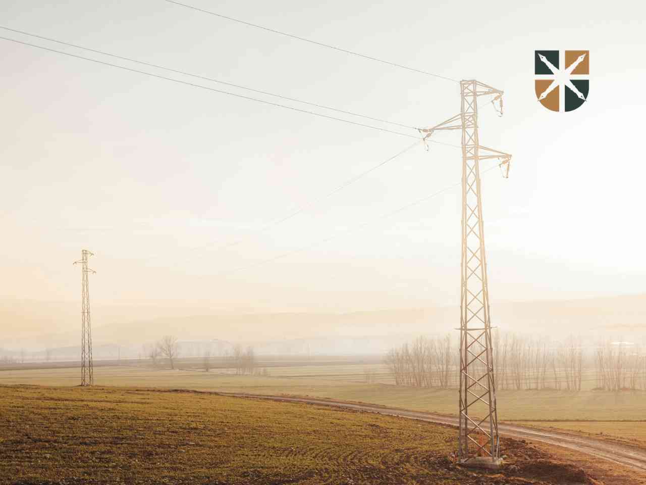 Metalowy słup i napowietrzna linia energetyczna na tle zamglonego pola – ilustracja ograniczeń w zabudowie działki.