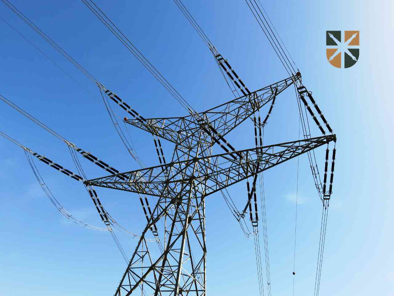 Szczyt stalowego słupa energetycznego z przewodami wysokiego napięcia na tle bezchmurnego, niebieskiego nieba.
