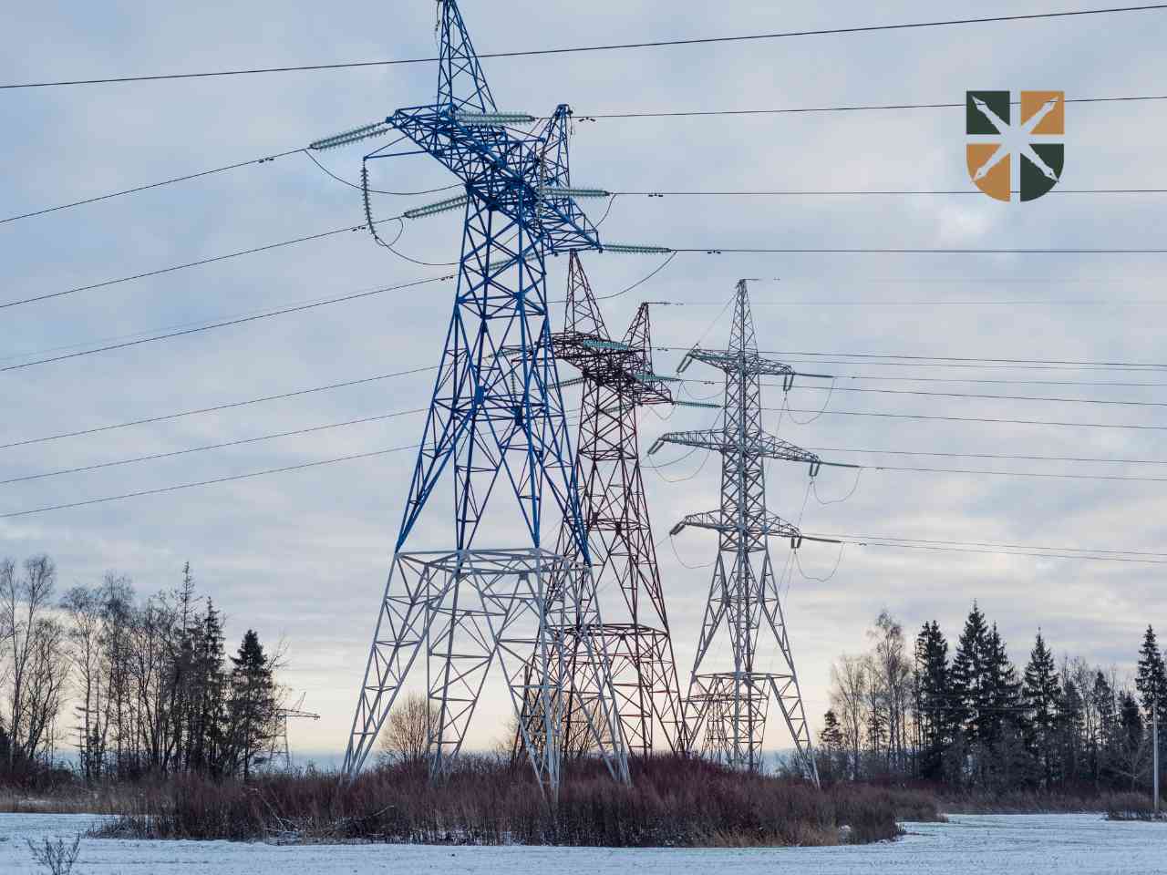 Trzy wysokie słupy energetyczne na ośnieżonym polu jako element infrastruktury przesyłowej.