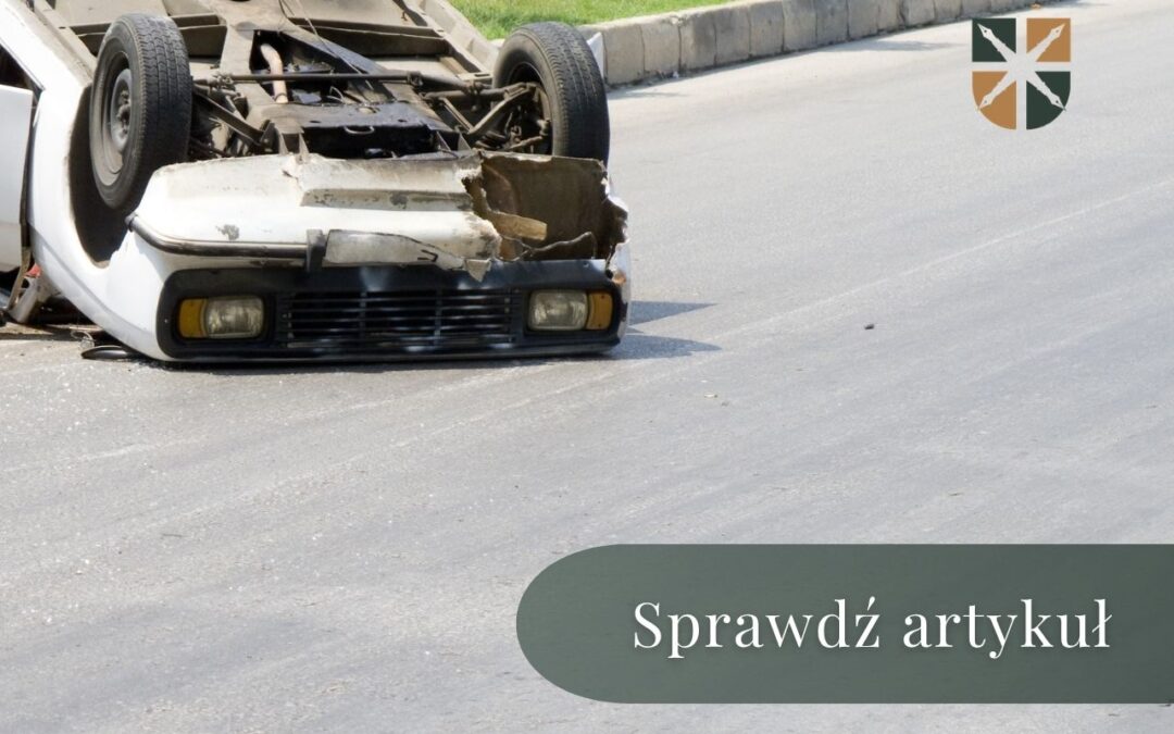 Biały samochód osobowy leży kołami do góry na asfalcie po wypadku drogowym.