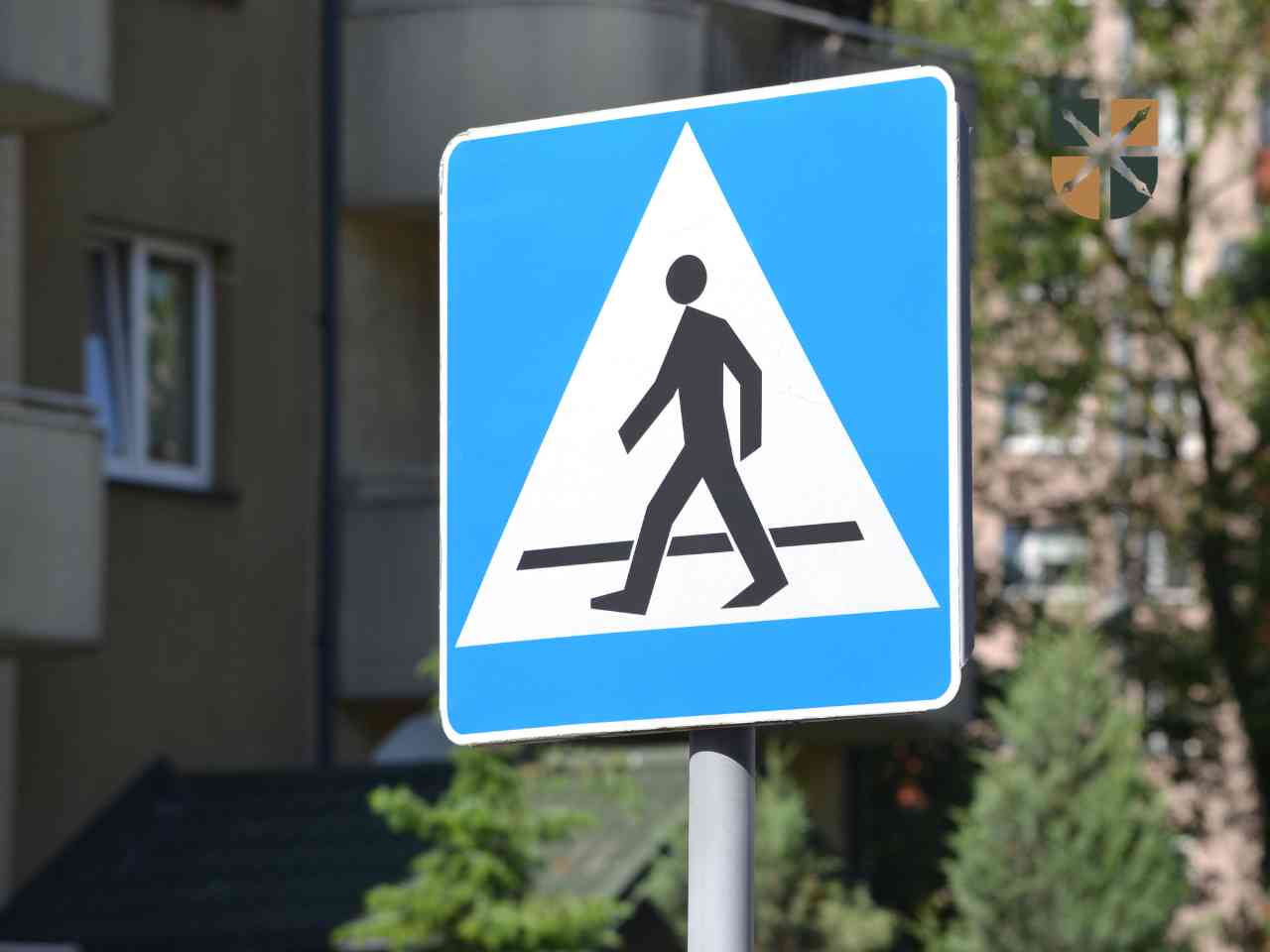 znak-przejscia Niebieski drogowy znak pionowy informujący o przejściu dla pieszych na tle miejskiej zabudowy.