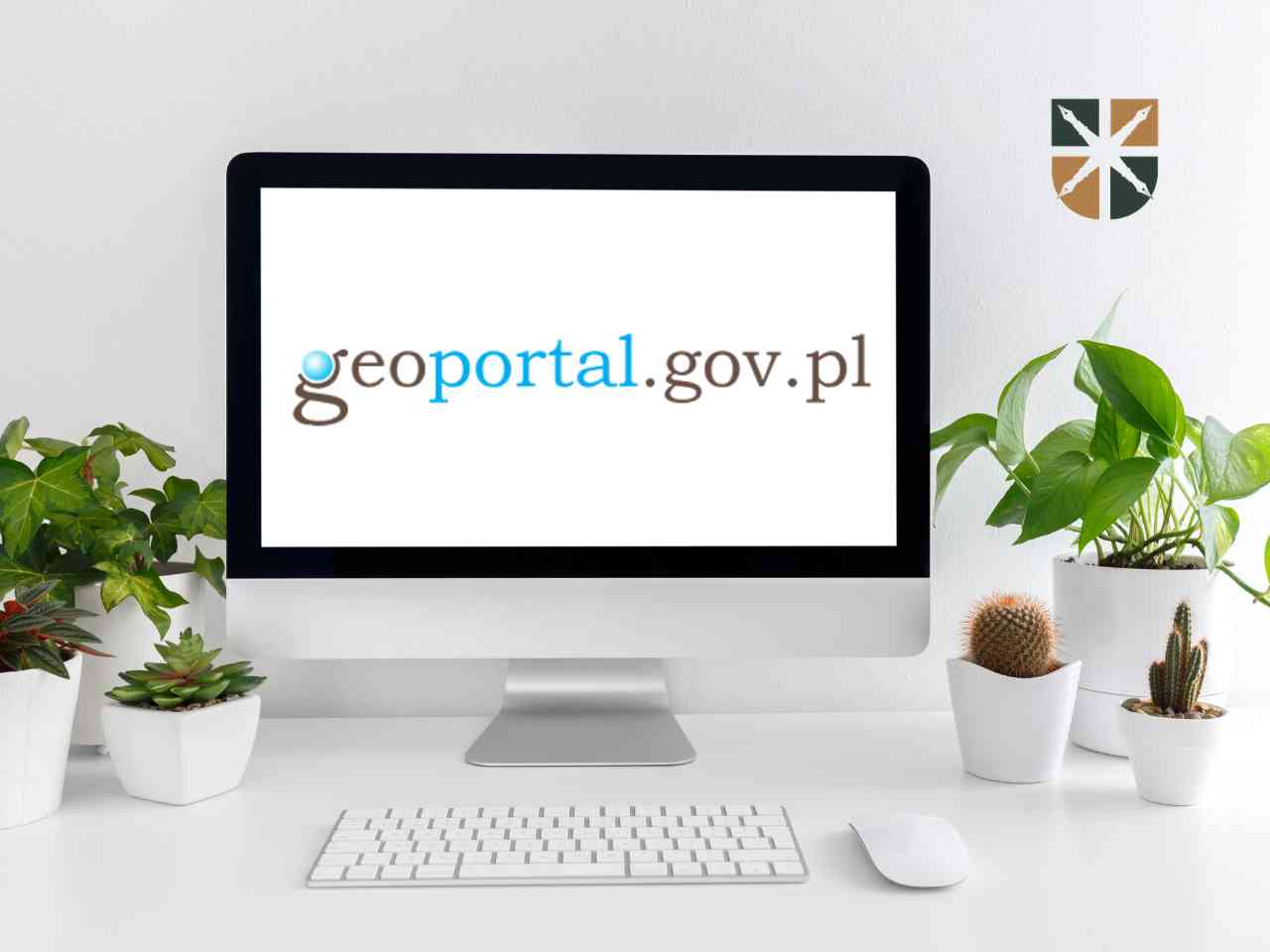 Monitor komputera z wyświetloną stroną główną serwisu geoportal.gov.pl na białym biurku obok roślin.