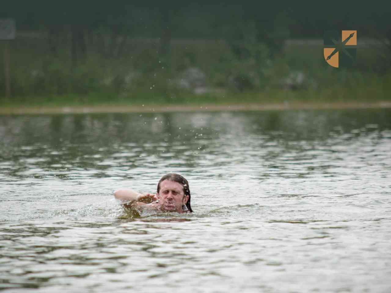 plywanie Man swimming in a lake with head and arm breaking the surface, water splashing around him, with a forested shoreline in the background