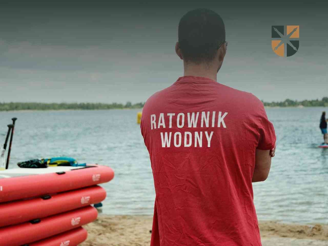 Ratownik wodny w czerwonej koszulce nadzorujący bezpieczeństwo kąpiących się osób na plaży.