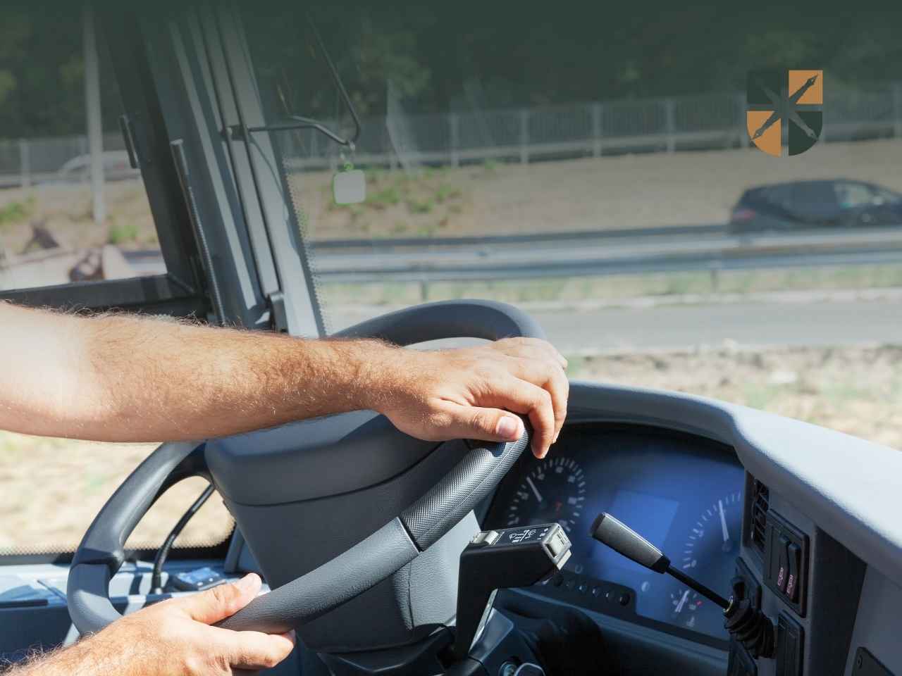 Driver's hands on the steering wheel inside a large vehicle cockpit, dashboard and gear lever in view