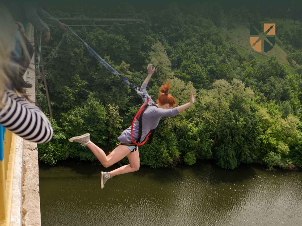Kobieta w uprzęży skacze na bungee z mostu nad rzeką. W rogu logo kancelarii.