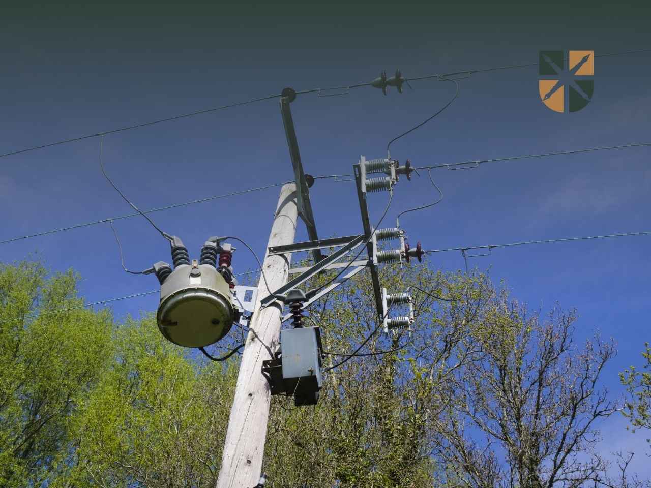 Drewniany słup energetyczny z transformatorem i przewodami niskiego napięcia na tle nieba.