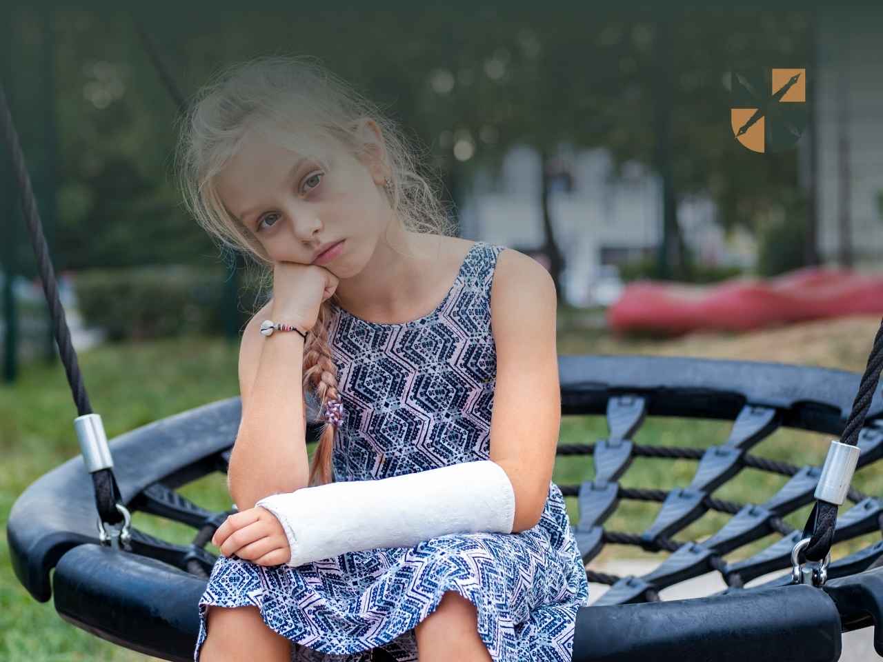 Smutna dziewczynka na huśtawce z ręką w gipsie po wypadku w szkole.