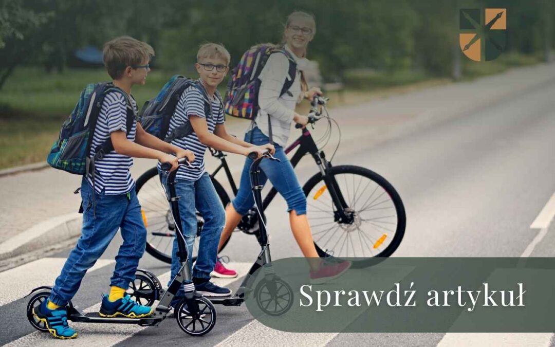 Trójka dzieci z plecakami przeprowadza rowery i hulajnogi przez przejście dla pieszych.