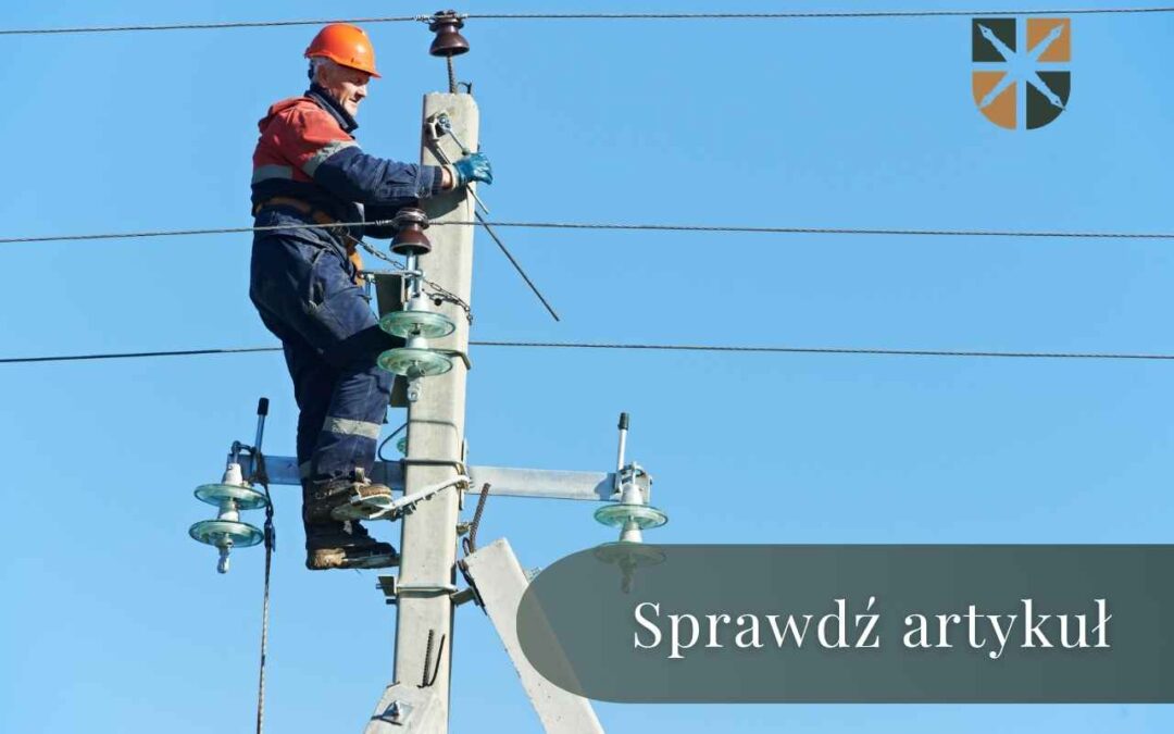 Elektryk w kasku wymienia elementy instalacji na drewnianym słupie energetycznym.