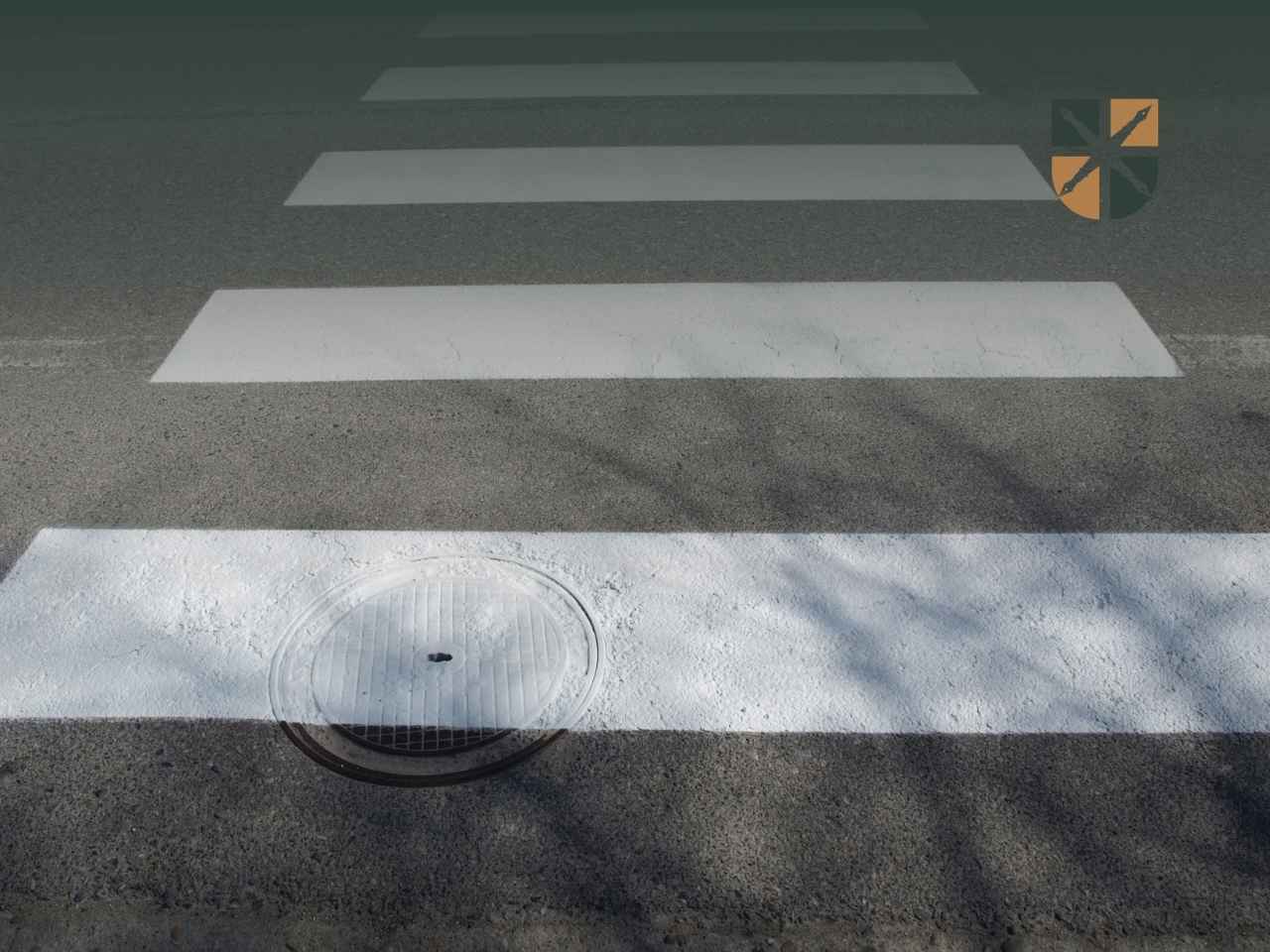 zebra Oznakowane przejście dla pieszych namalowane na asfalcie wokół włazu kanalizacyjnego.