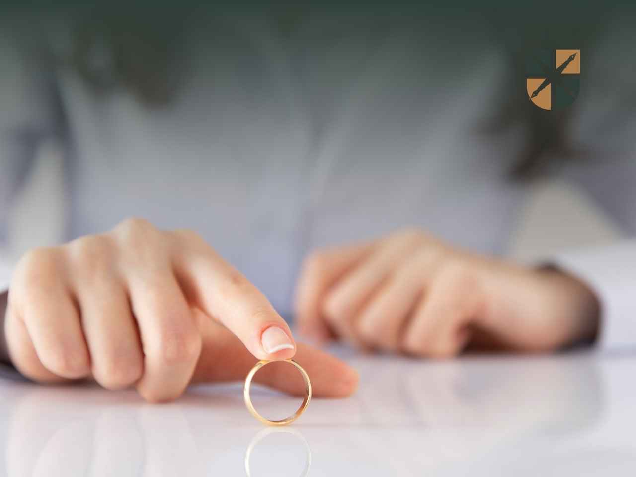 Dłoń kobiety dotykająca zdjętej złotej obrączki ślubnej na stole.